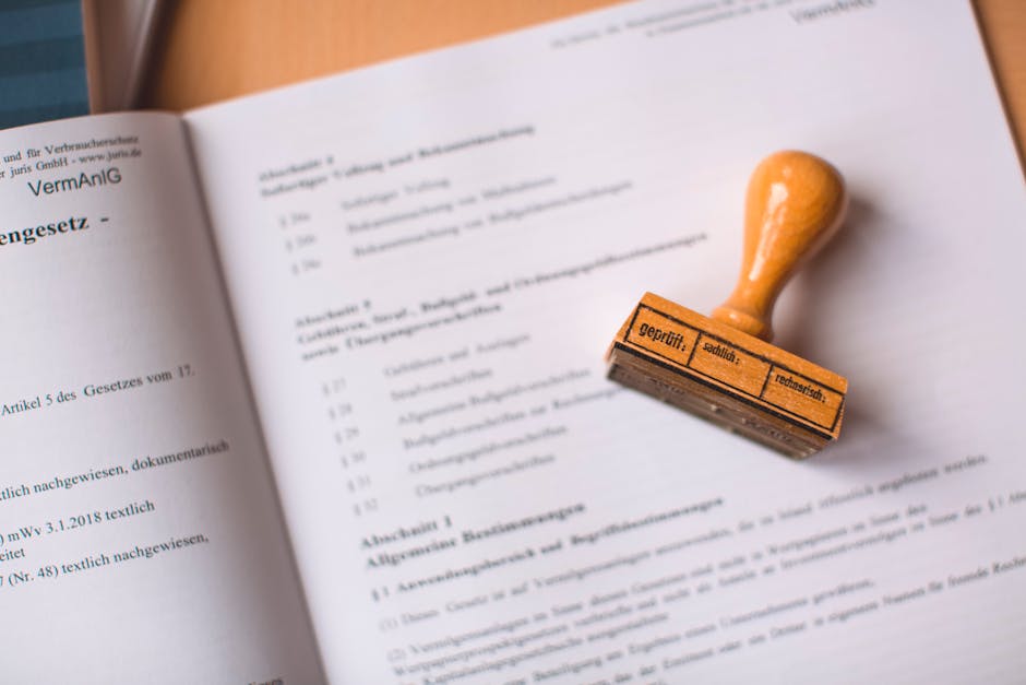 A close-up photograph of a legal or official document with printed text, partially visible and laid open on a flat surface. Resting on the right side of the paper is a rubber stamp with a wooden handl